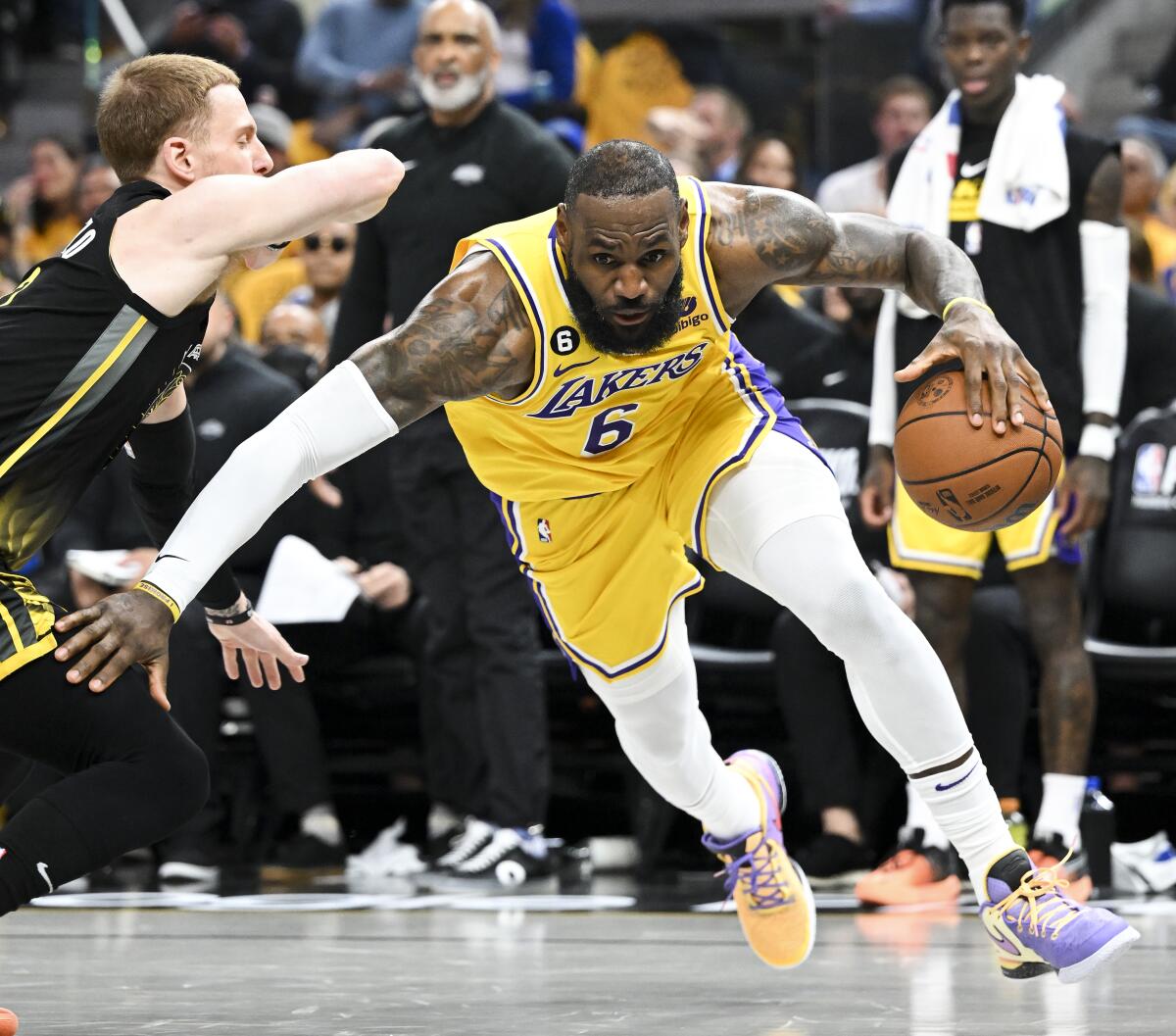 Lakers forward LeBron James leaning down and dribbling around Warriors guard Donte DiVincenzo 