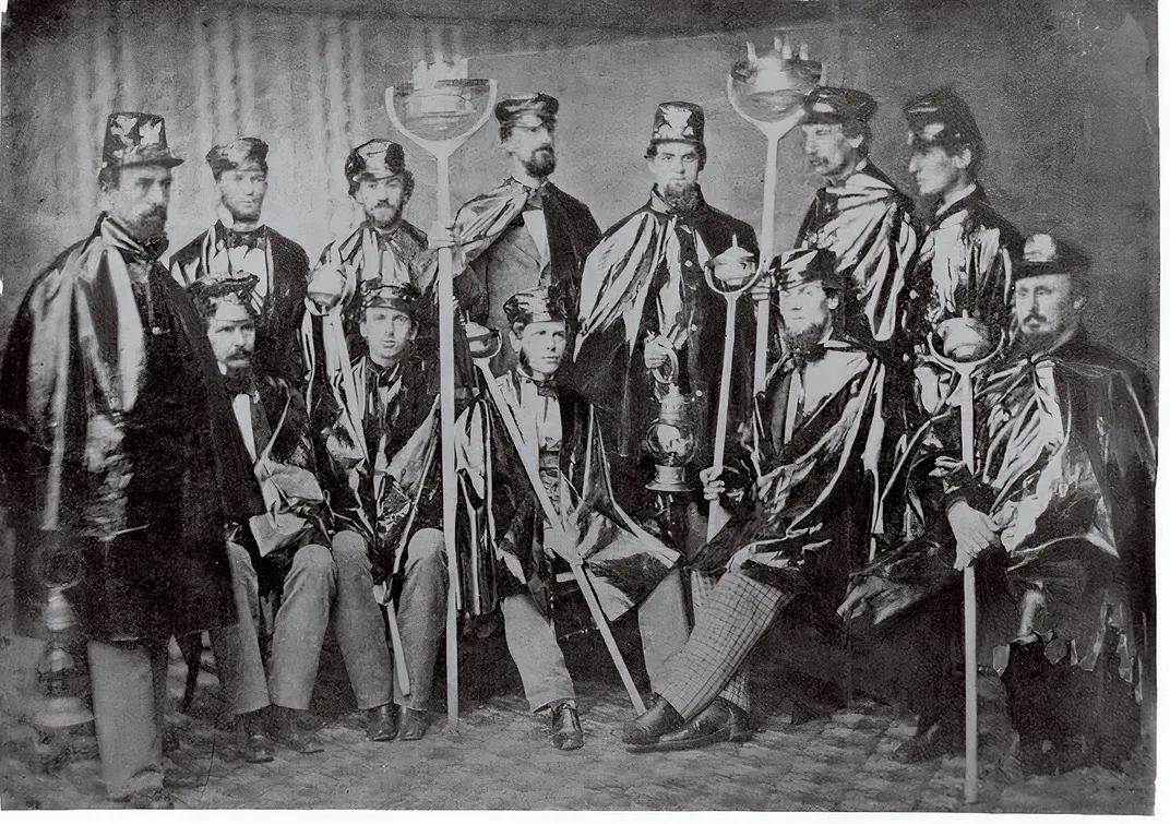 a group of men in caps holing oil lamps sit for a portrait