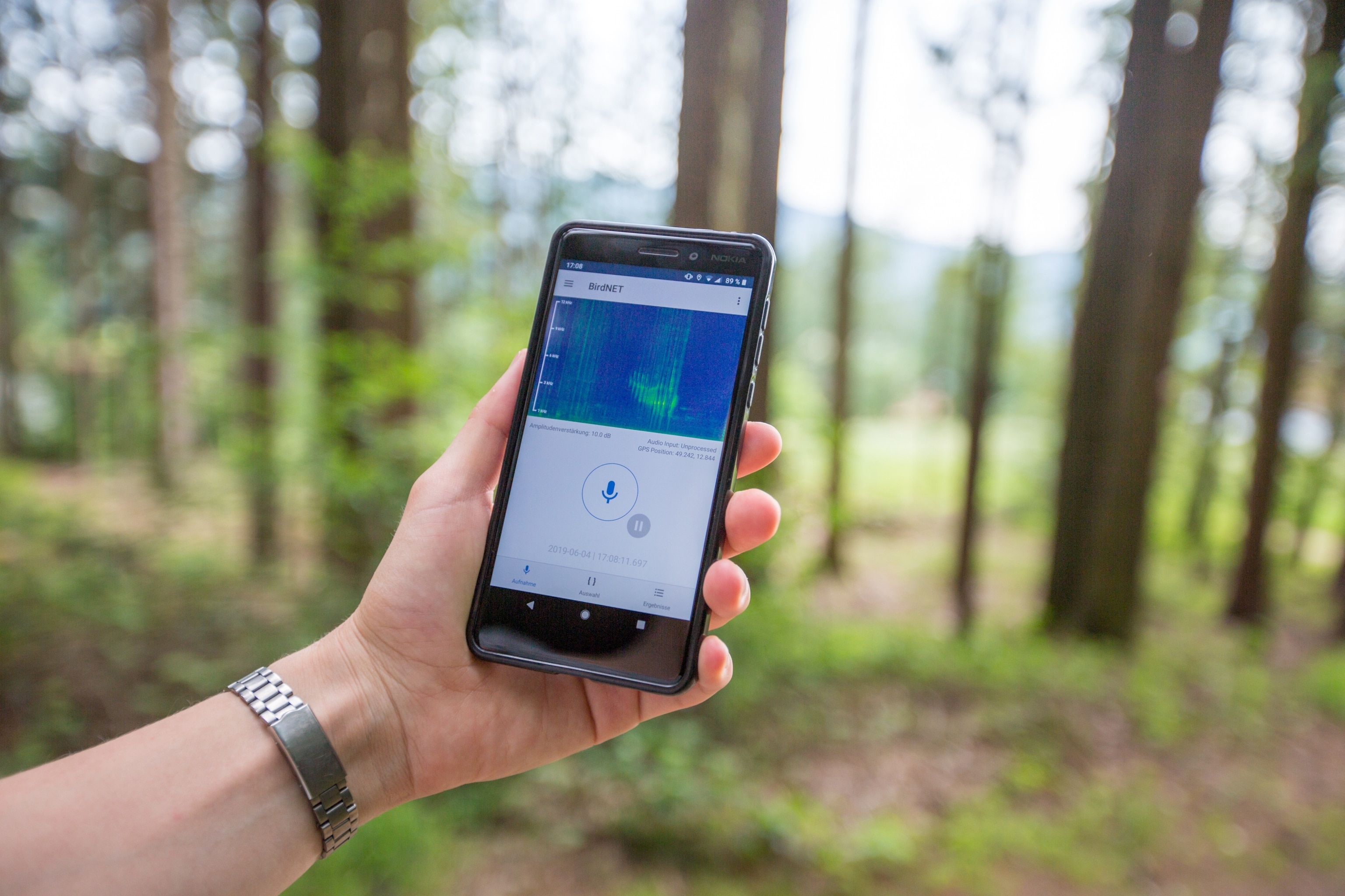 A hand holding a phone and displaying the us of an app sound waves appear on the phone screen.