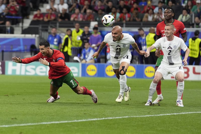 Slovenia's Vanja Drkusic, center, heads the ball as in action with Portugal's Cristiano Ronaldo, left, during a round of sixteen match between Portugal and Slovenia at the Euro 2024 soccer tournament in Frankfurt, Germany, Monday, July 1, 2024. (AP Photo/Ariel Schalit)
